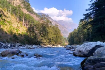 A picture of a river flowing through a village in Kasol with mountains on both sides