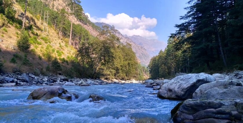 A picture of a river flowing through a village in Kasol with mountains on both sides