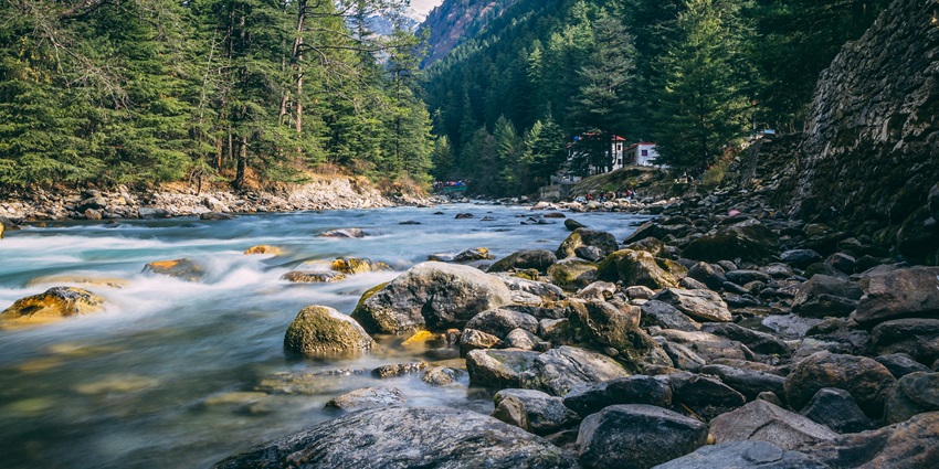 A scenic landscape featuring lush greenery, azure waters, and rocky cliffs in Kasol.