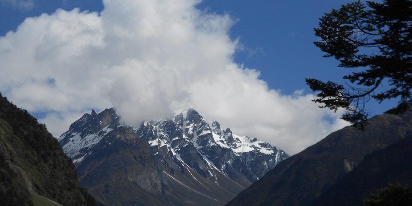 A distant view of the snow-covered Mount Katao in Sikkim from a lush green valley