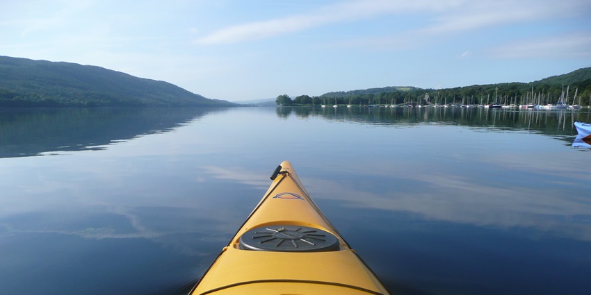 A kayak floating in water with a vast view of the river with hills on both sides, on a sunny day
