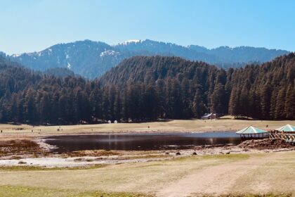 An image of Khajjiar Lake is surrounded by trees and green meadows in Himachal Pradesh.