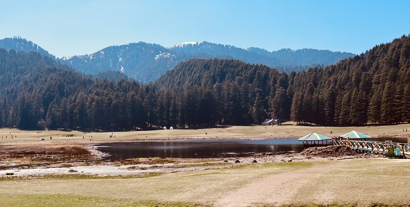 An image of Khajjiar Lake is surrounded by trees and green meadows in Himachal Pradesh.