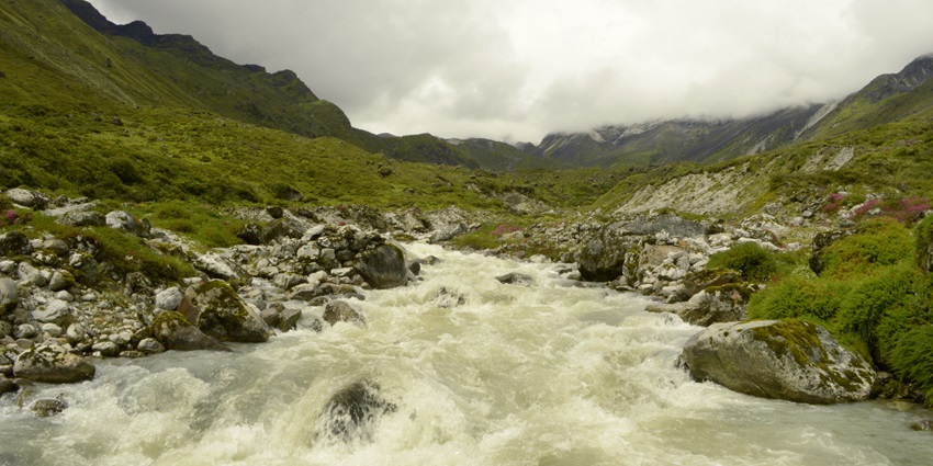 A picture of a small river flowing from the middle of a grassy terrain on a bright day