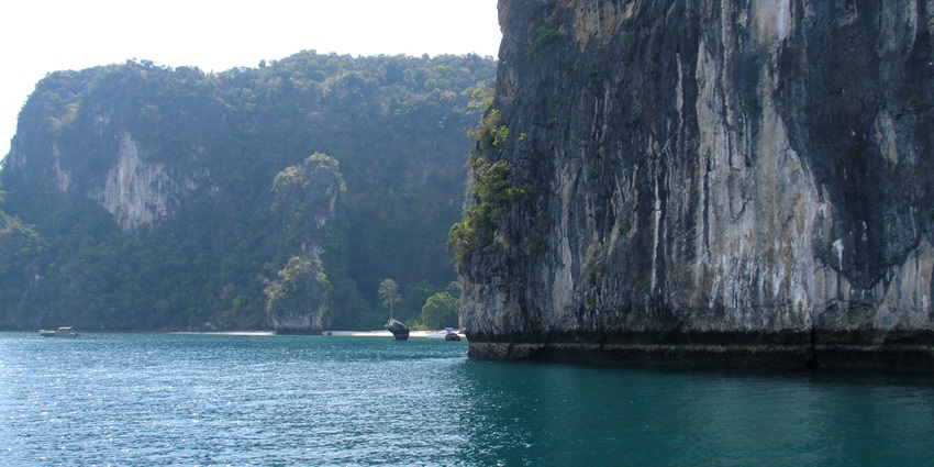 A picture of boats sailing next to a huge hill-like island nearby a perfect spot for snorkelling in Phuket