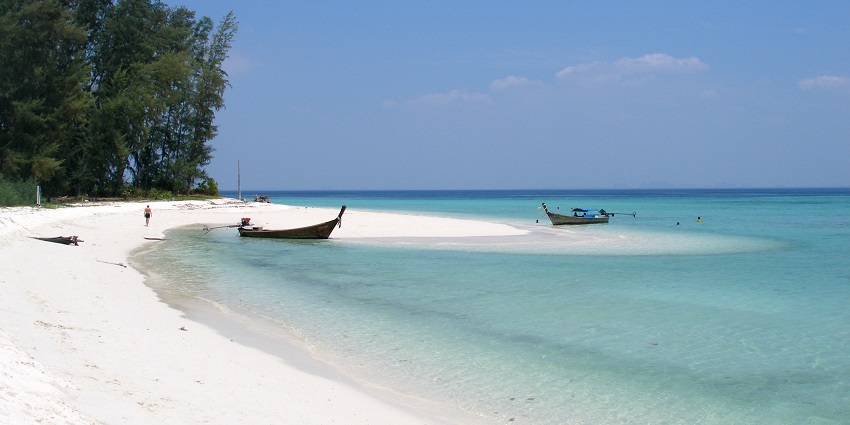 A crescent style beach with boats and sea on the right side and trees on the left side