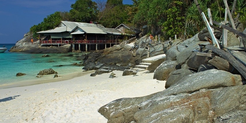 A picture of an island with big rocks and a wood-made resort by the sea shore