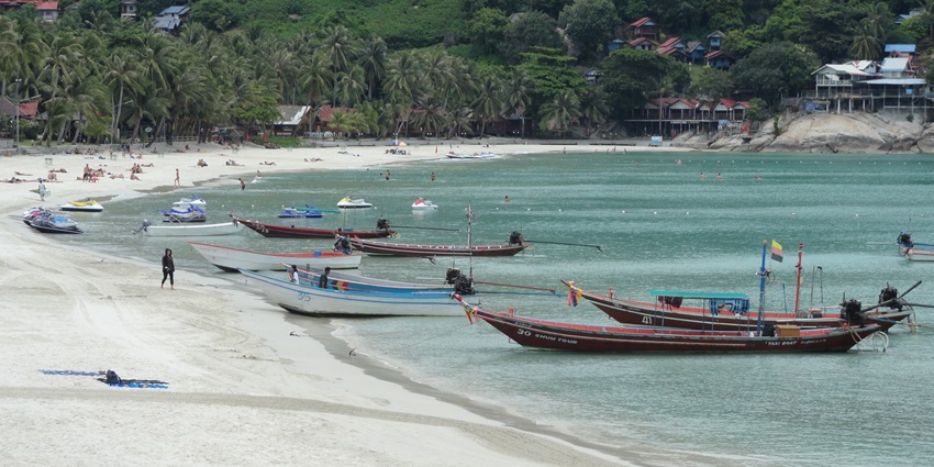 A picture of a beach with multiple boats and ferries parked and people enjoying the serene environment