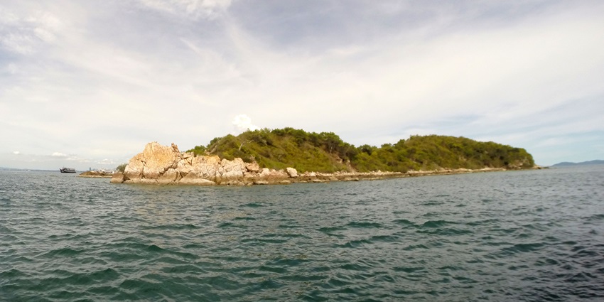 A distant picture of a rocky island in the middle of a sea on a bright sunny day