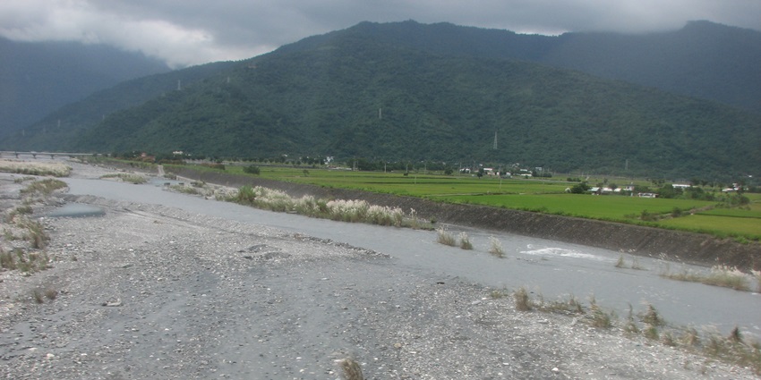 Image of a river in between the mountains and a village on the side during day time view