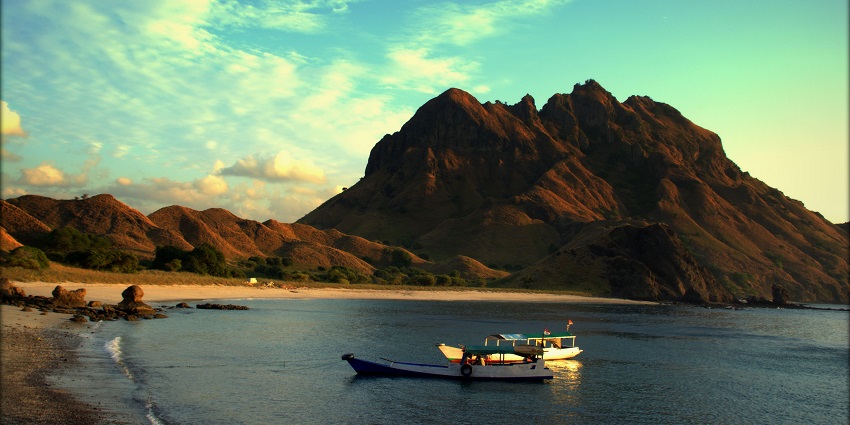 A picture of an island with a mountain in the background and a boat approaching the shore