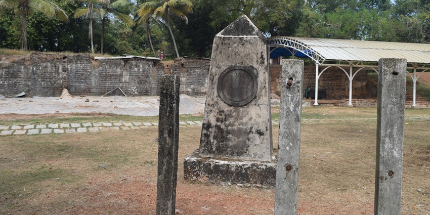 A picture of a ruined memorial pillar in a fort complex with a shed in the background