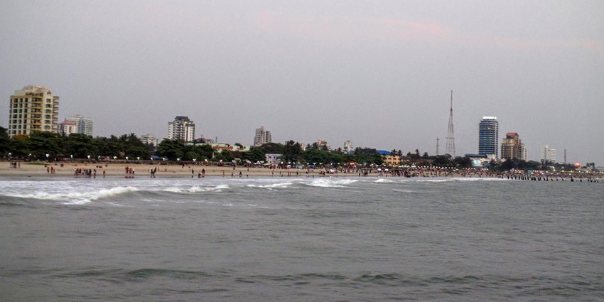 A picture of the Kozhikode Beach coastline, with trees and buildings in the background