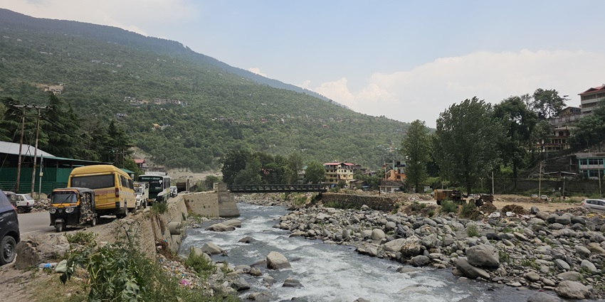 A picture of a river flowing through a hill station with rocks and pebbles all around