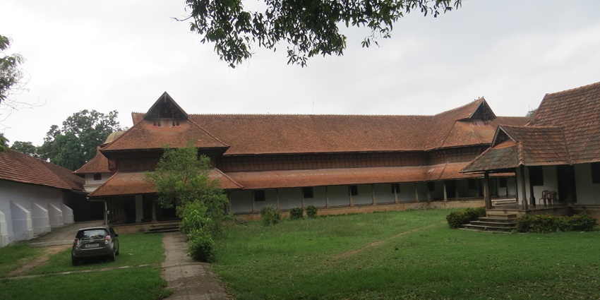 A picture of a traditional palace in Trivandrum with a large garden area in front of it