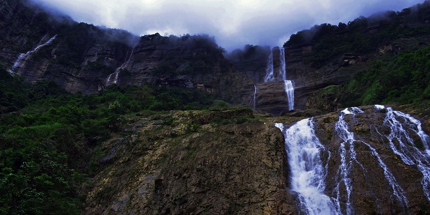 An enchanting view of Kynrem Falls flowing through lush green meadows under a cloudy sky.