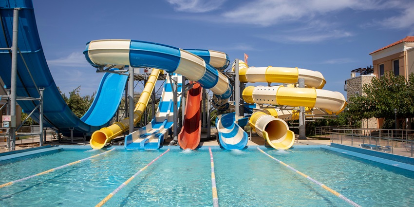 A view of a blue and yellow water slide with a pool in a water park during the daytime.