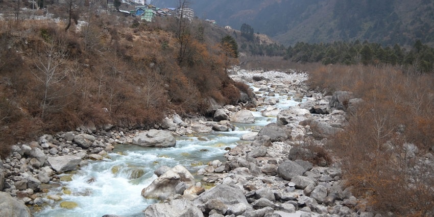 A picture of a small river with pebbles flowing through a valley between two green hills