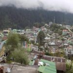 A picture of a hill town showing trees and houses with tall mountains in the front