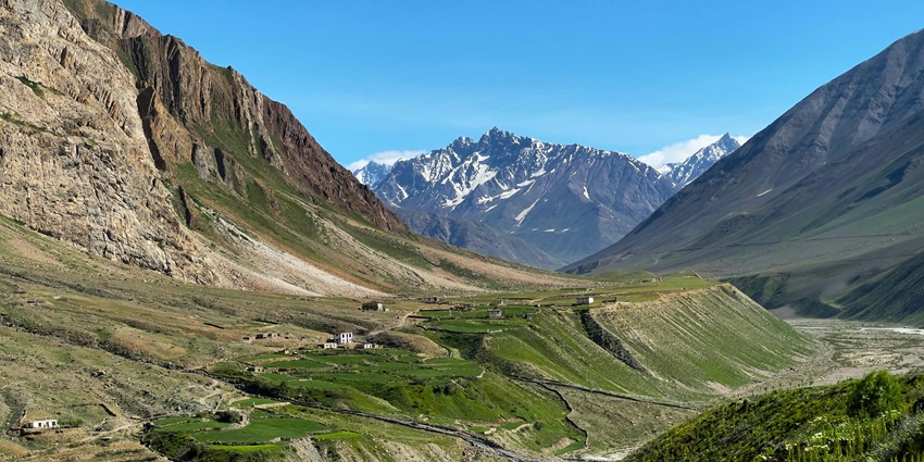 Scenic view of verdant landscapes amidst mountain ranges with snow capped hills beyond