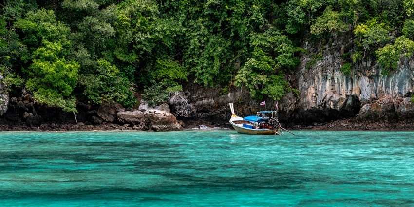A boat sailing in a water body with a tall mountain-like island in the background
