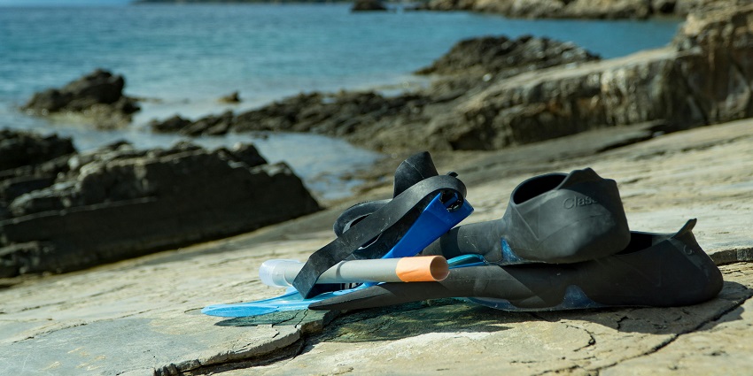 A picture of snorkelling gear kept on a rock with a sea and mountains in the background
