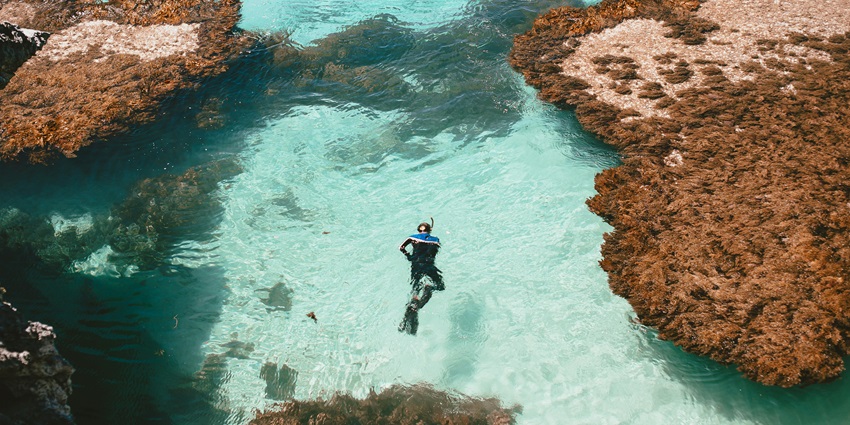 A picture of a man snorkelling in a water body surrounded by rocky islands