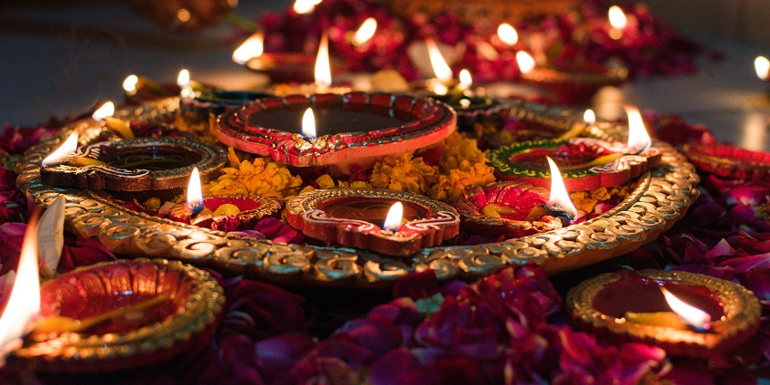 Image of beautifully lighting and decorated diyas on a plate and flowers on the side.