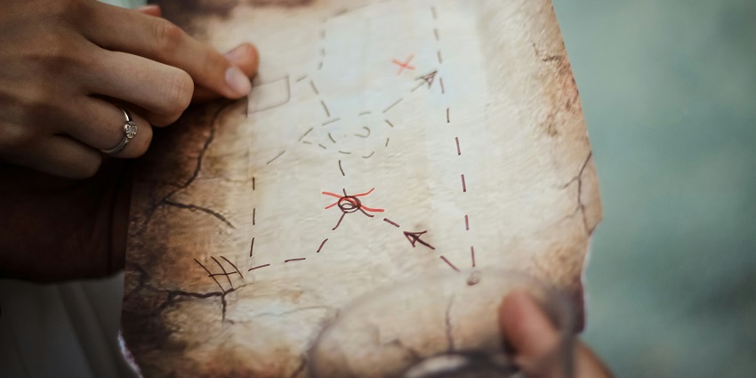 A selectively focused view of a hand holding a brown map with black and red lines.