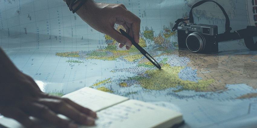 A fantastic view of a world map with a person’s hand holding a pen over it with a camera.