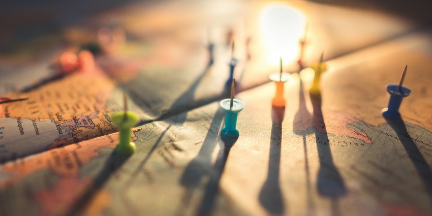 A selectively focused view of a map with assorted push pins on top of it during the day.