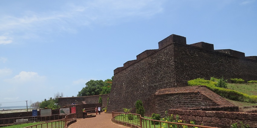 A picture of a walkway in a fort in Kannur with gardens on both sides and a scenic landscape