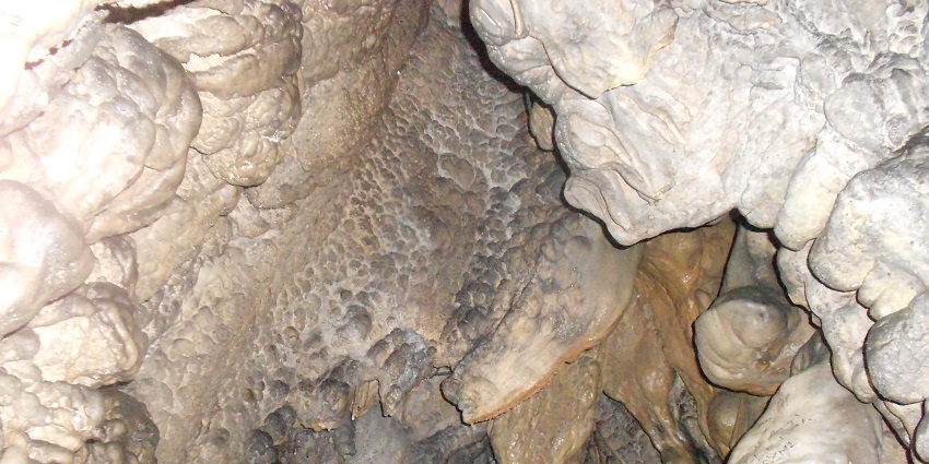 A picture of a stone-made cave entrance in Meghalaya with people exploring the insides using torch and lights