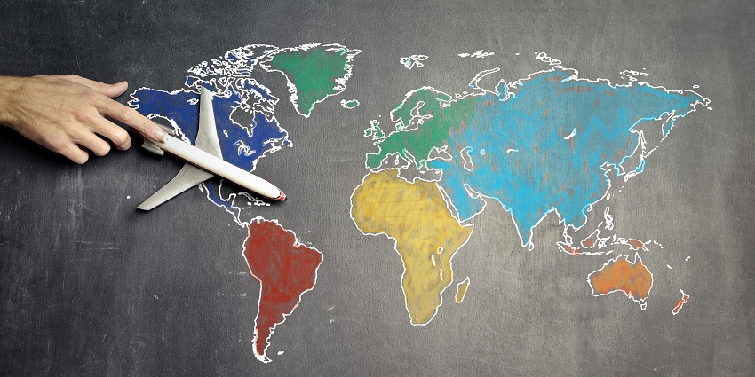 A view of a hand holding a toy plane in front of a blackboard with a colourful world map.