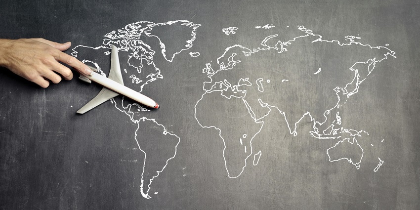 A view of a miniature toy plane in a hand over a blackboard with a map drawn on it.