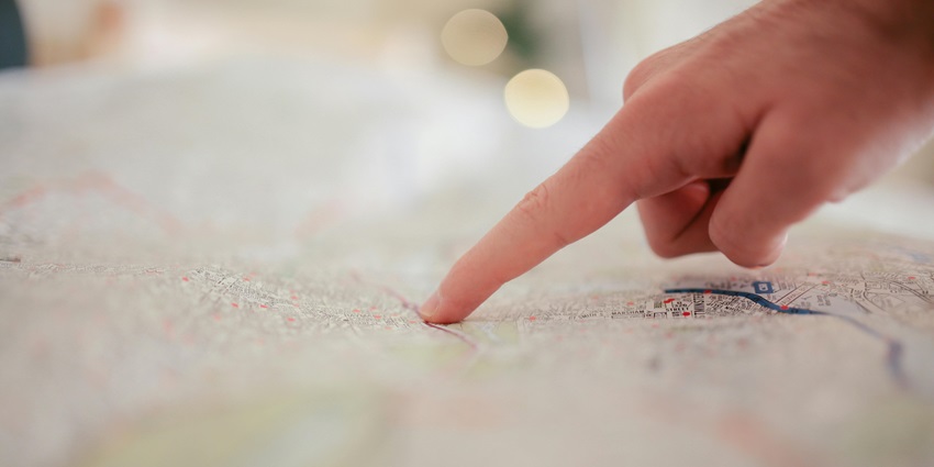 A selectively focused view of a person’s finger pointing on a white map on a table.