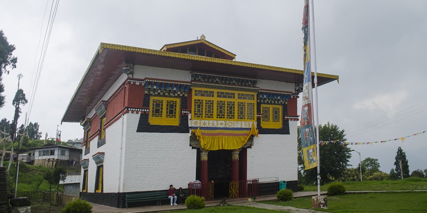 A view of a Monastery with white, red and golden architecture with a flagpole in front.
