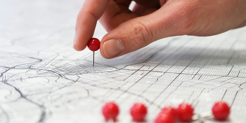 A selectively focused view of a red push pin on a black-and-white map used to navigate.