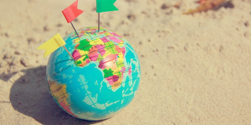 A selectively focused view of a globe with colourful pins on the sand during the daytime.