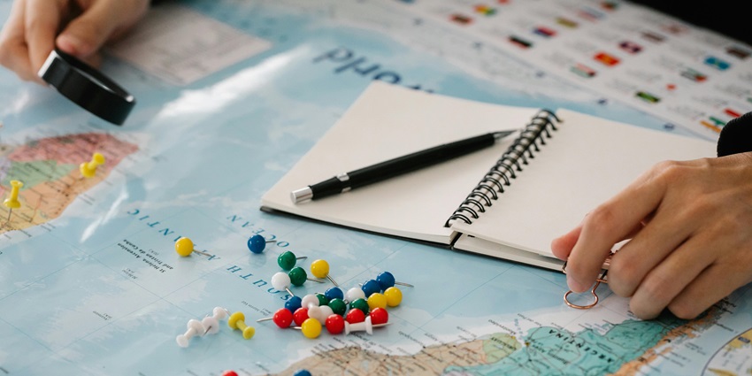 A selectively focused view of a colourful map with assorted push pins on top of it.