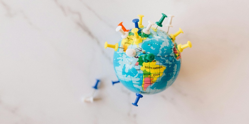 A selectively focused view of a colourful globe with assorted push pins on it on a table.