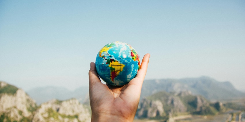 A selectively focused view of a person’s hand holding a colourful globe in the day.