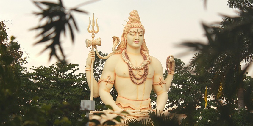 Image of Lord Shiva statue surrounded by trees in a calm environment under clear sky.