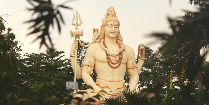 Lord Shiva's statue stands tall amidst vibrant trees, creating a tranquil atmosphere.