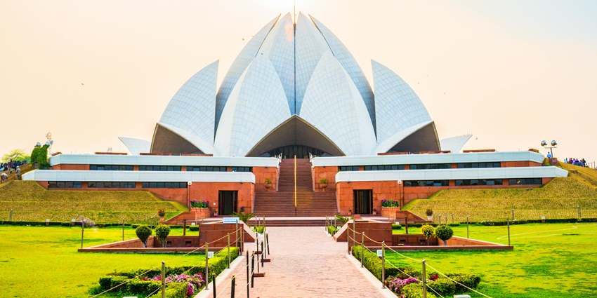 Lotus Temple with white marble petals surrounded by green lawns under clear blue sky.