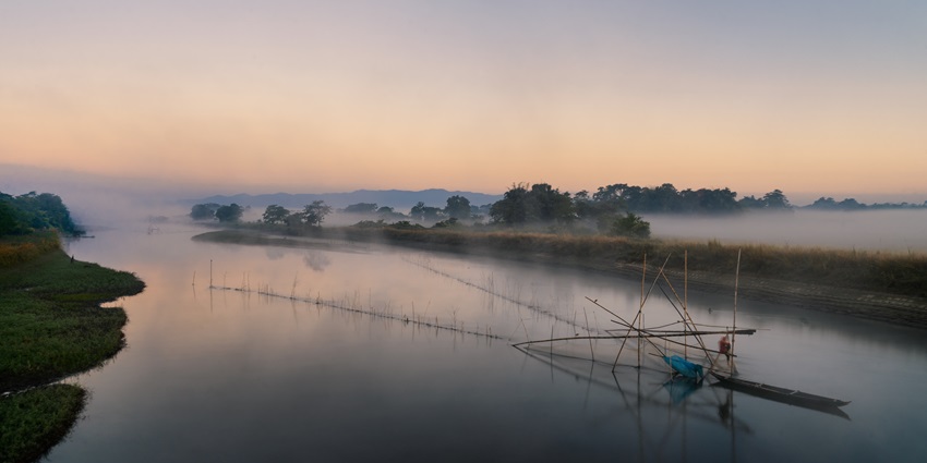 Fisherman stands in shallow water, skillfully managing a cast net at serene riverbank