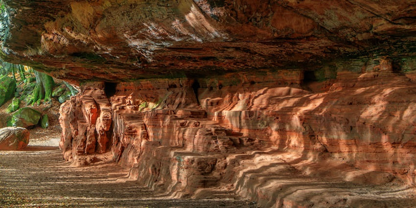 A picture of a cave entrance in Shillong under a massive hill, surrounded by greenery