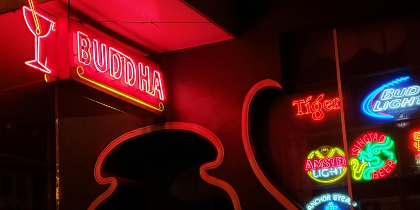 Neon sign of a bar in red and white, glowing brightly in the dark.