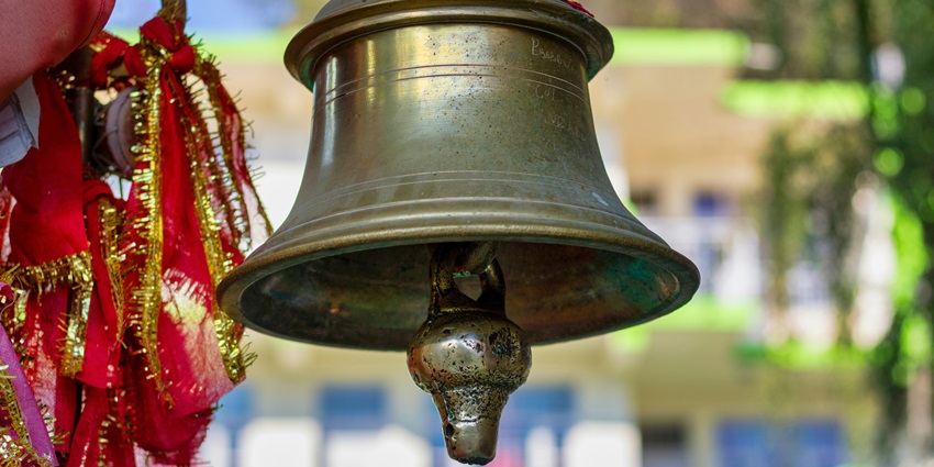 A breathtaking view of a golden bell in a temple in front of red pieces of clothes.