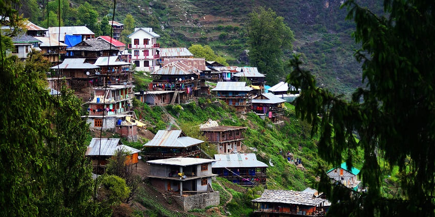 An aerial view of a verdant village in Himachal Pradesh with wooden houses all around